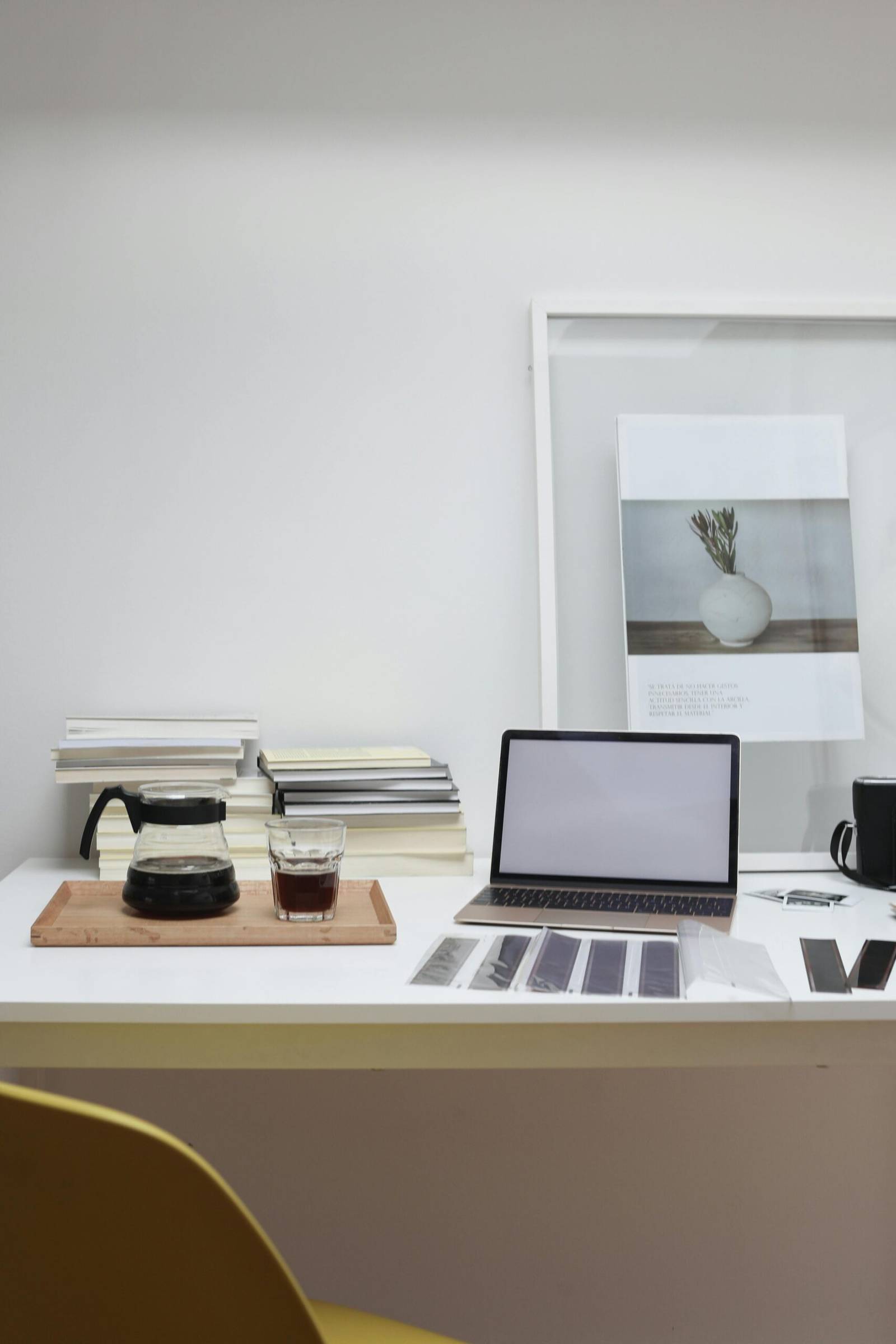 Working desk with laptop reversal film tapes and framed photo arranged with coffee glass and pot and books stack
